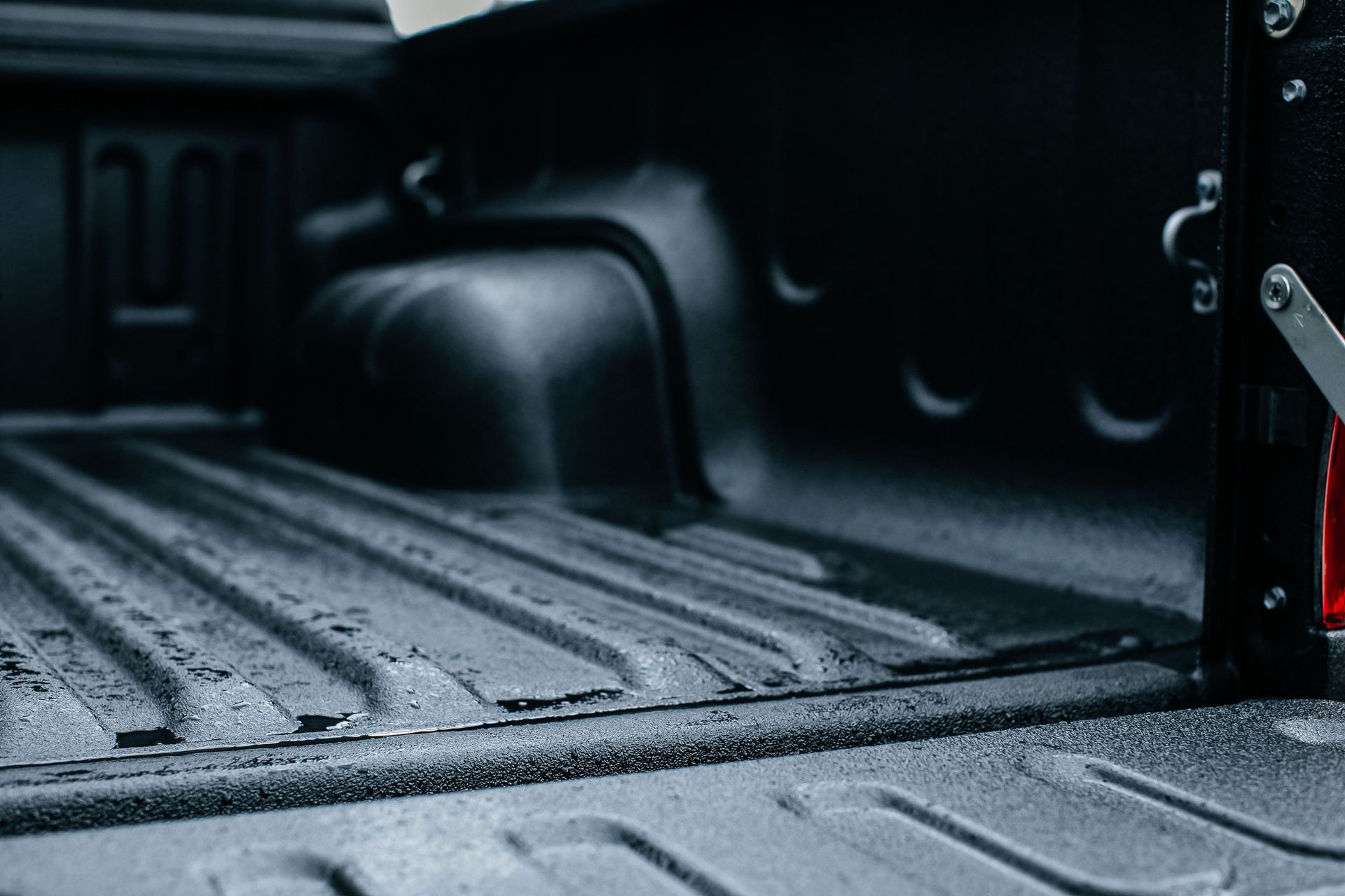 Black pickup truck bed with textured, rain-speckled liner and a red tail light visible at the side