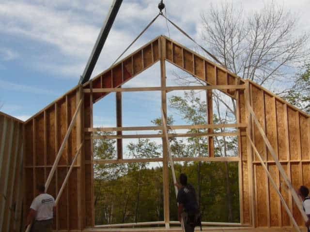 Des ouvriers du bâtiment utilisent une grue pour mettre en place une grande charpente de pignon en bois dans le cadre d'un projet de construction de maison.