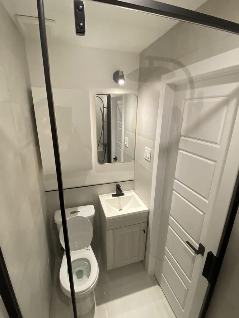 Une petite salle de bains moderne avec des toilettes blanches, un meuble-lavabo avec lavabo et un miroir rectangulaire sur des murs gris clair.
