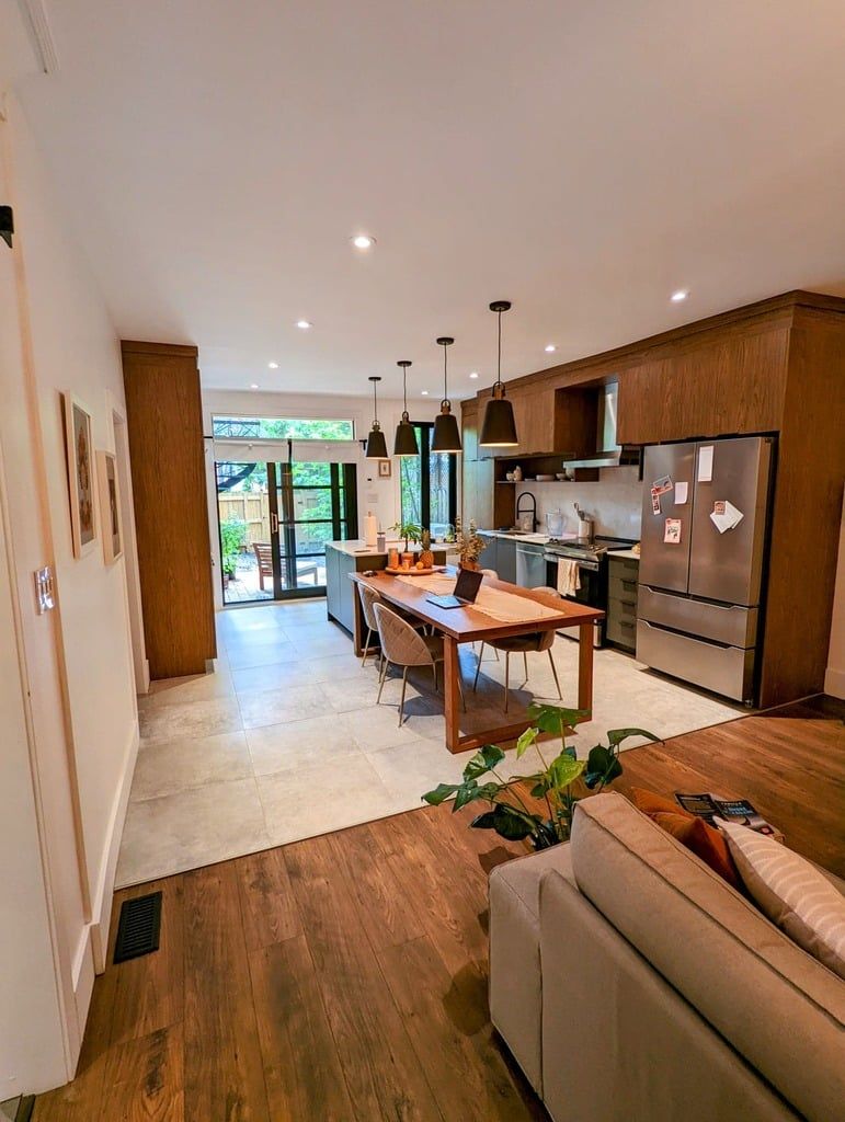 Cuisine et salle à manger à aire ouverte avec armoires en bois, électroménagers en acier inoxydable, planchers carrelés et vue sur la cour arrière.
