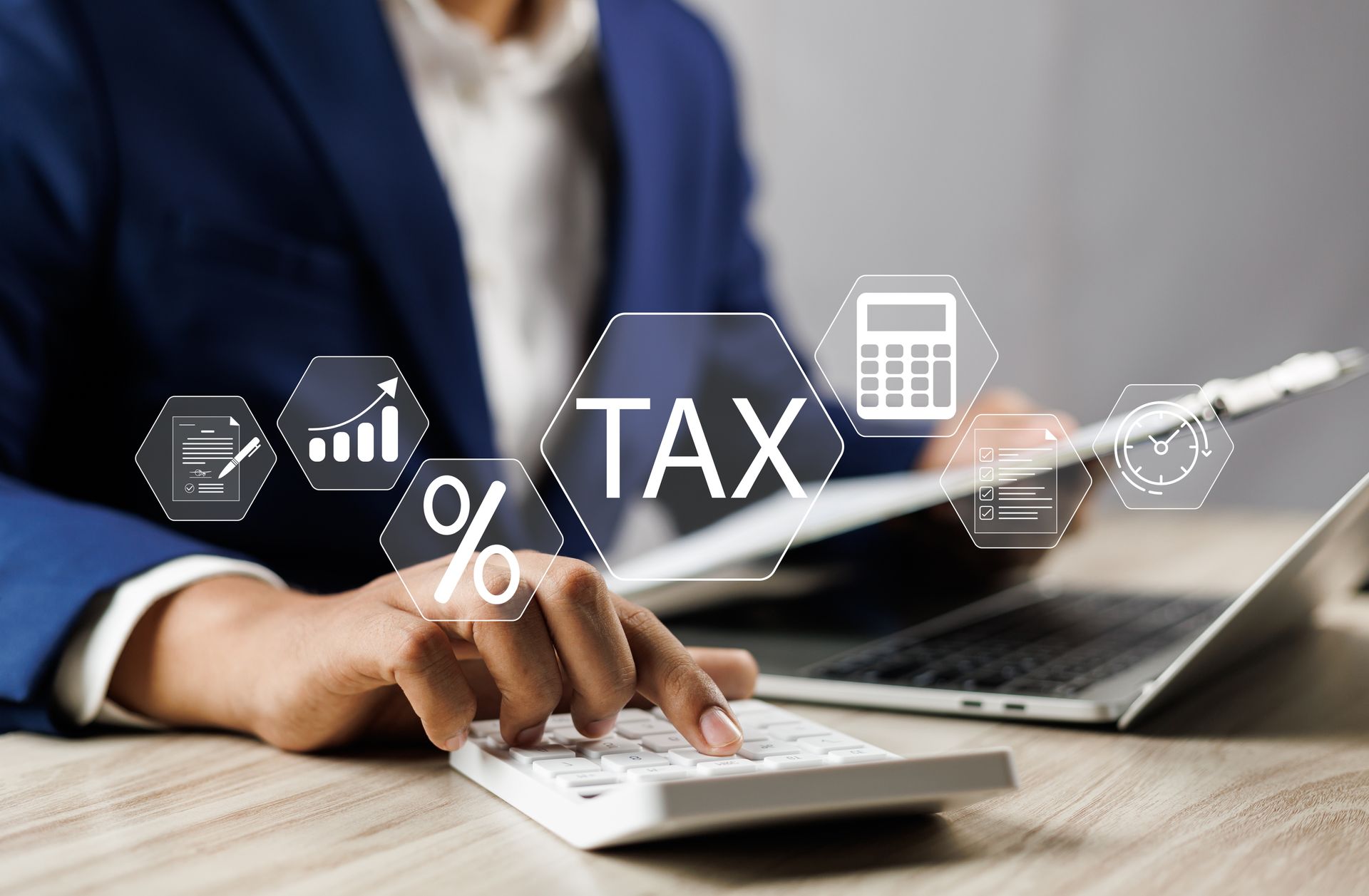 Businessperson using a calculator and laptop with tax icons overlayed on a desk