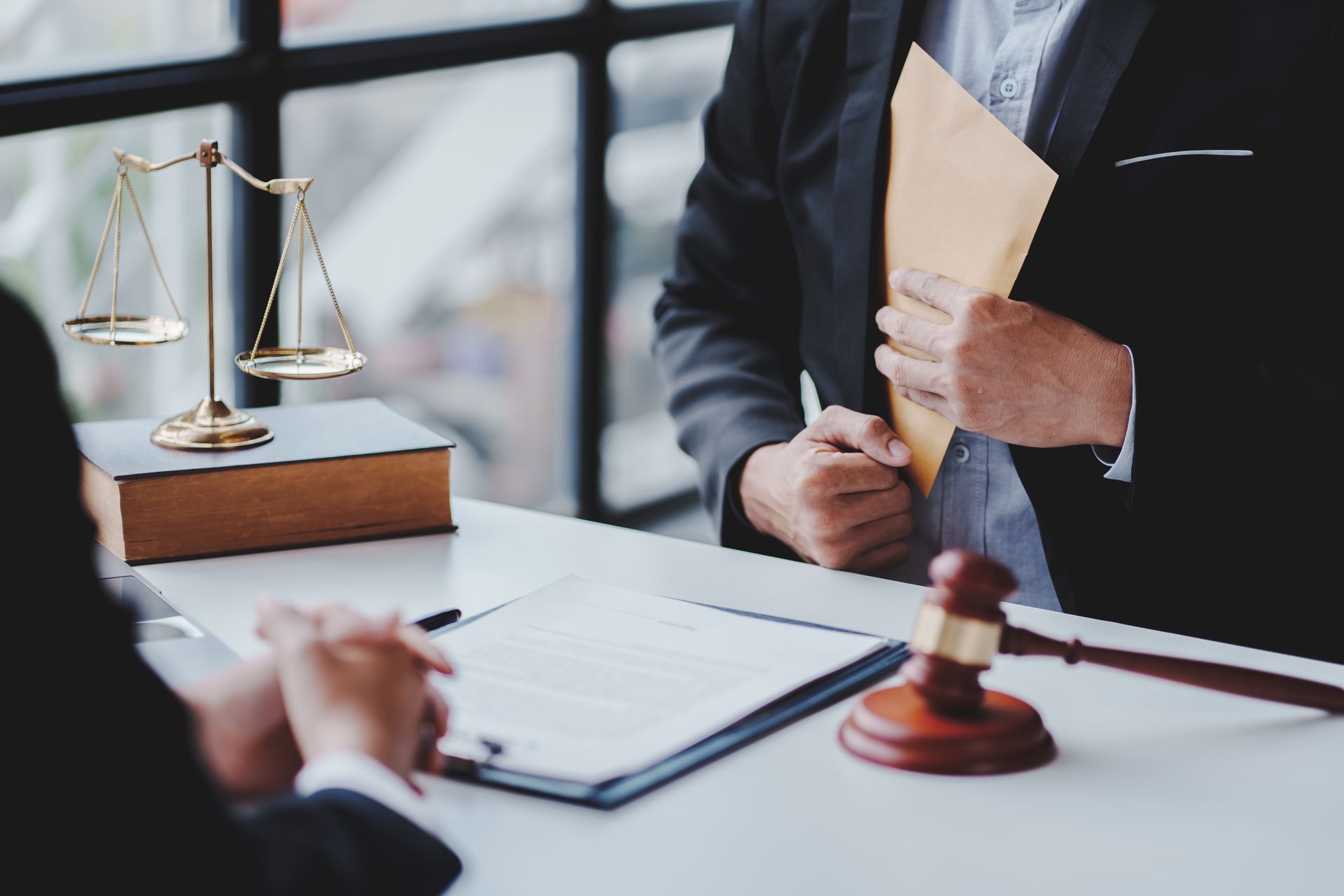 Lawyer in suit holding documents at desk with gavel and scales of justice in a courtroom setting