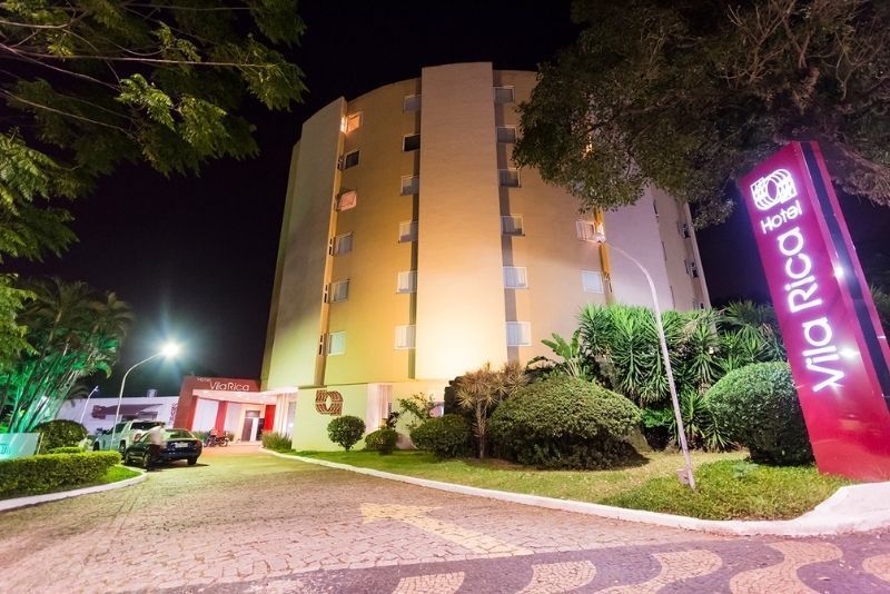 Vista noturna de um prédio de hotel amarelo com uma placa vermelha 