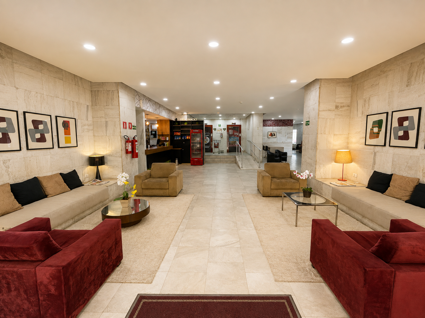 Entrada coberta com banco de madeira, tapete verde e passarela aberta à noite.