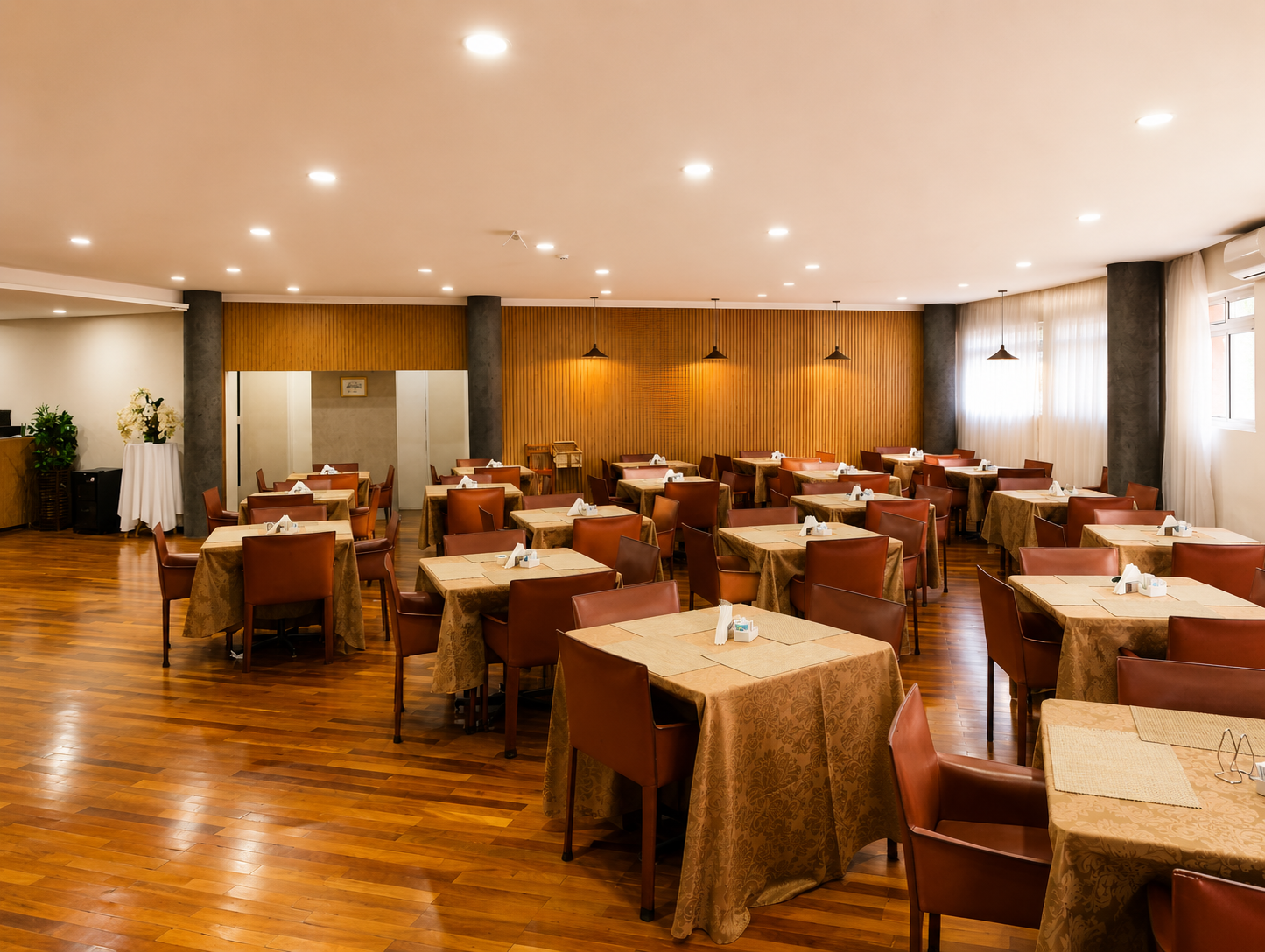 Pátio externo do restaurante com cadeiras de vime e mesas postas com vista para uma piscina iluminada e área verde.