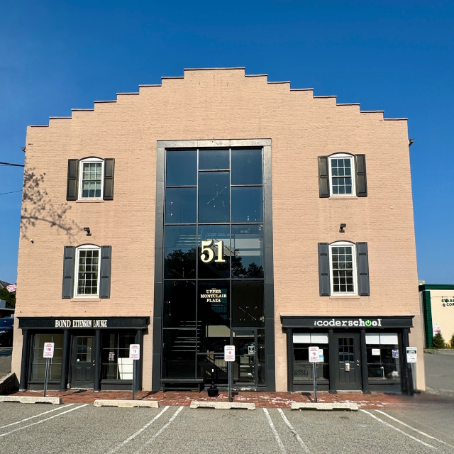 Building at 51 with a large glass front entrance, flanked by businesses, under a clear blue sky.