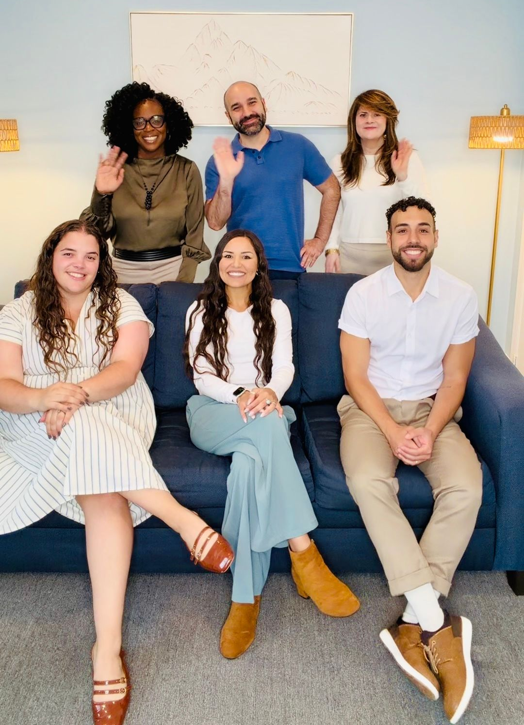 Six people sitting and standing in a bright living room, smiling for a group photo.