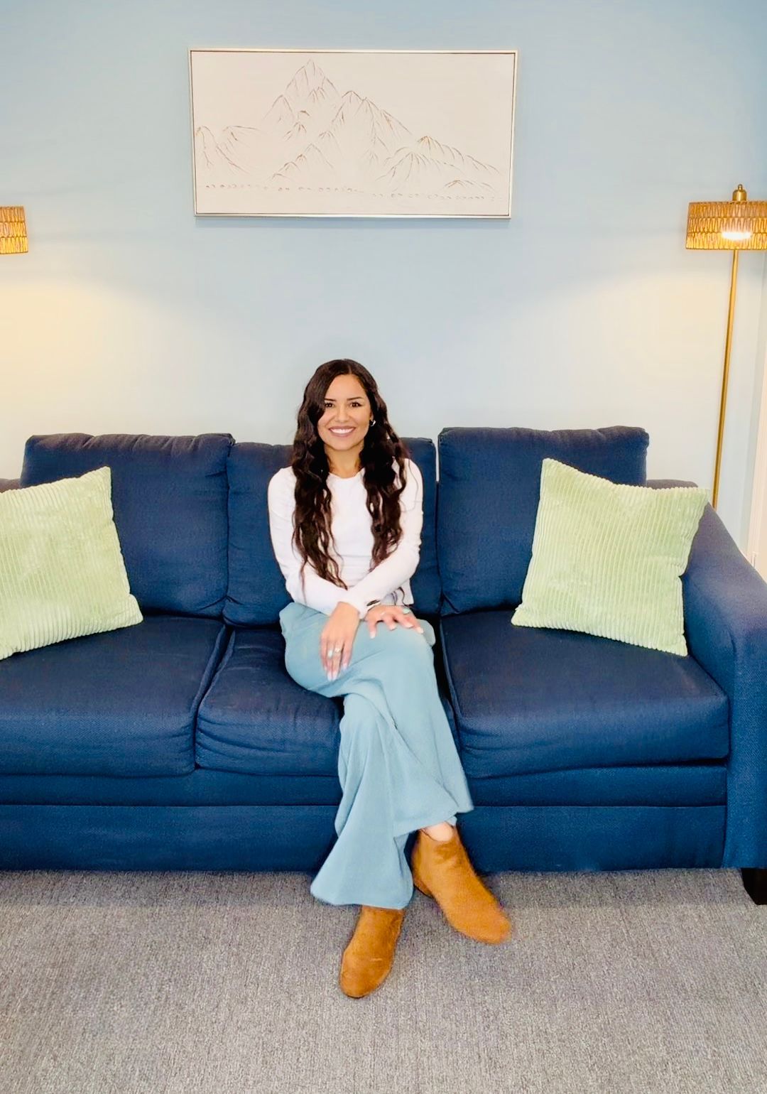 Woman sitting on a blue couch in a bright living room with a wall art above and floor lamps on both sides