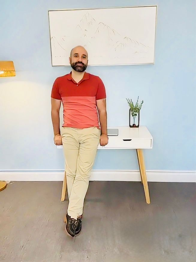 Man leaning against a white desk in a bright room with a whiteboard and small plant.