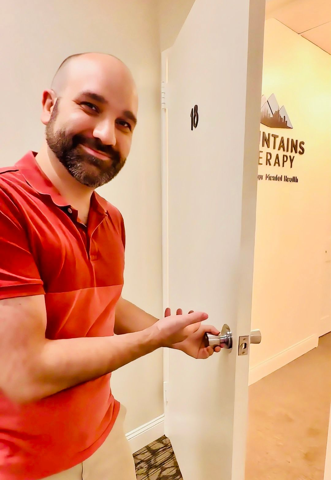 Smiling man in red shirt opening a white door in a hallway