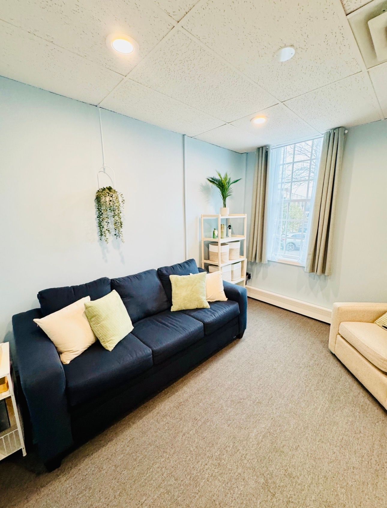 Bright living room with navy sofa, yellow pillows, beige carpet, and window seat by a tall window.