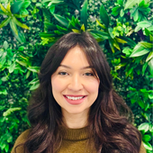 Portrait of a smiling woman with dark hair before a lush green leafy background