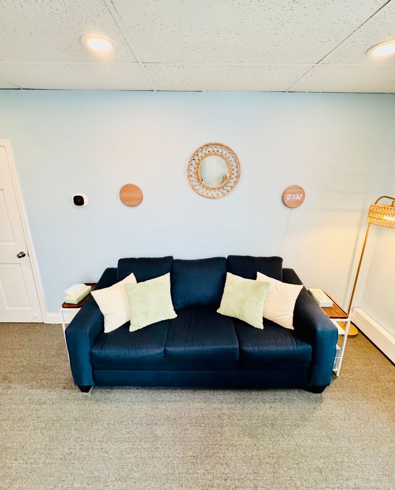 Blue sofa with white pillows in a light-blue living room, with wall decor and a floor lamp.