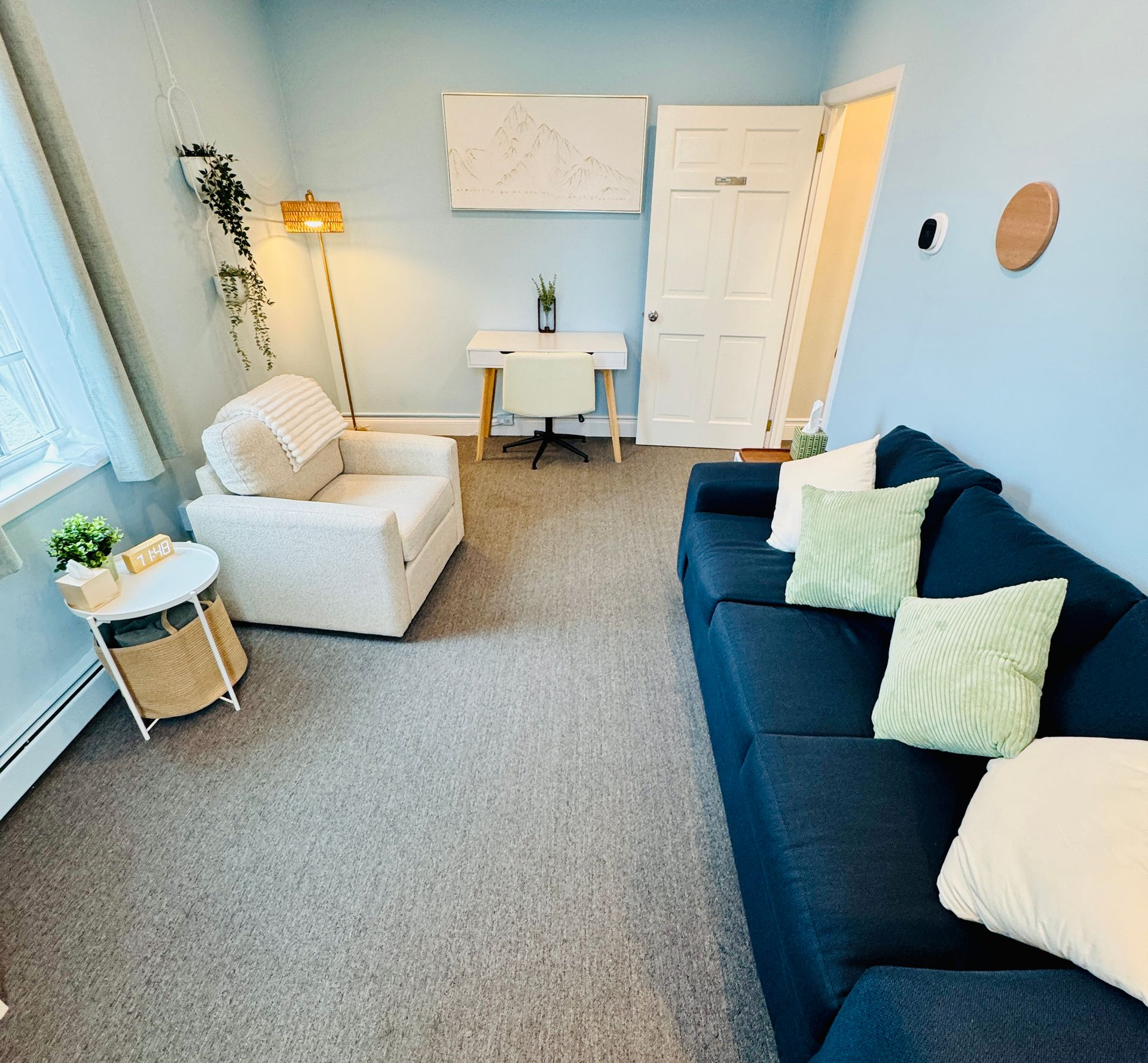 A light blue office with a navy couch, white armchair, and a desk.