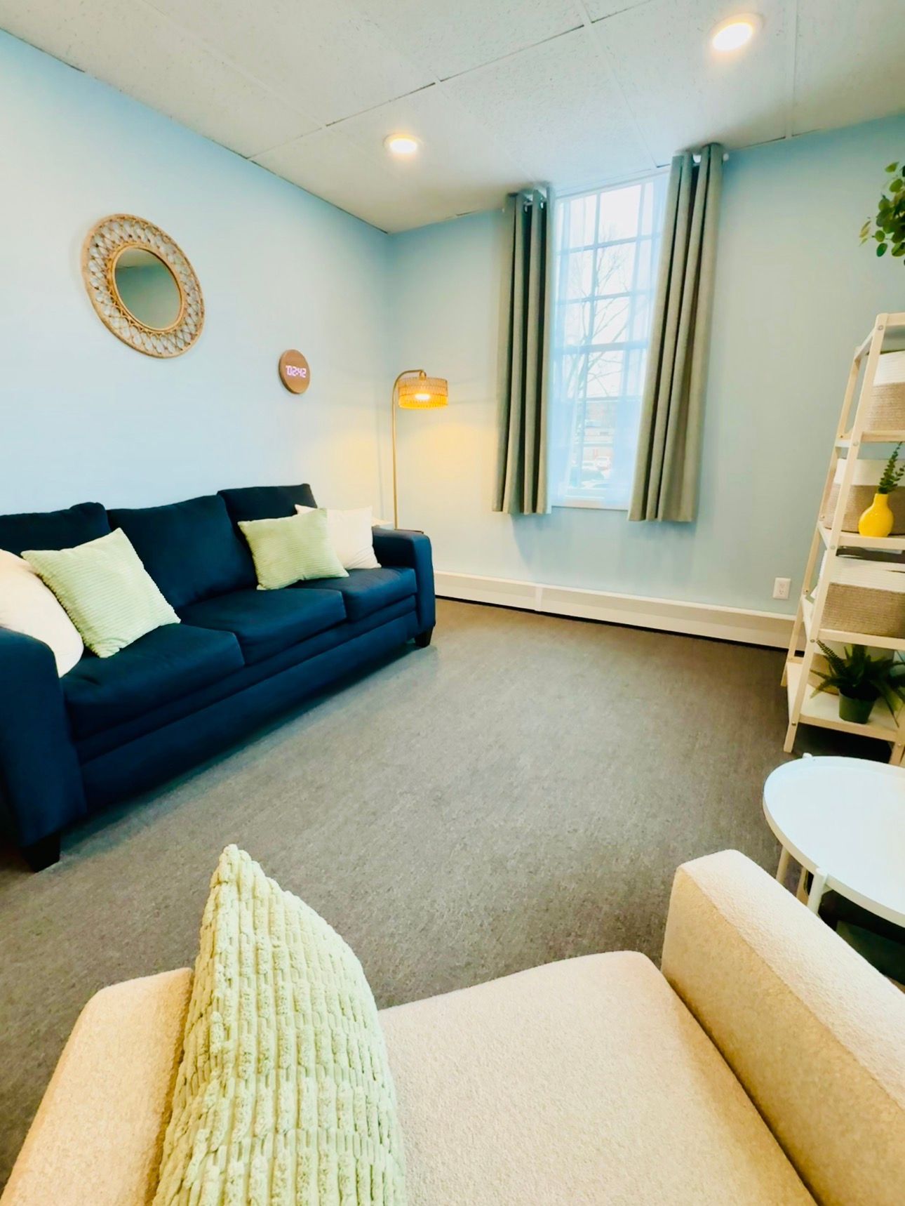 Bright living room with blue sofa, beige chairs, window with curtains, and light blue walls