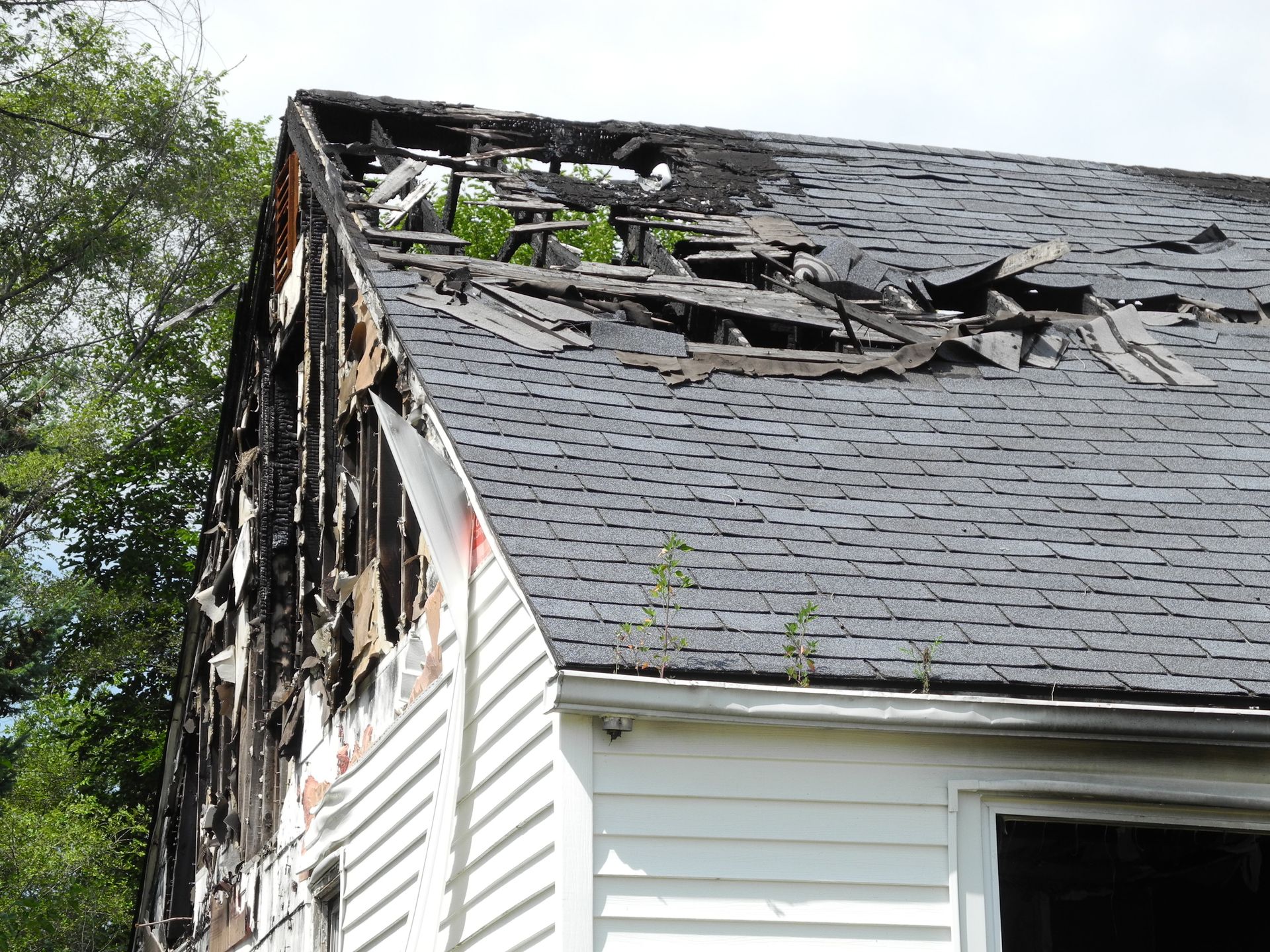Severely damaged house roof with missing shingles and exposed structure on one side.