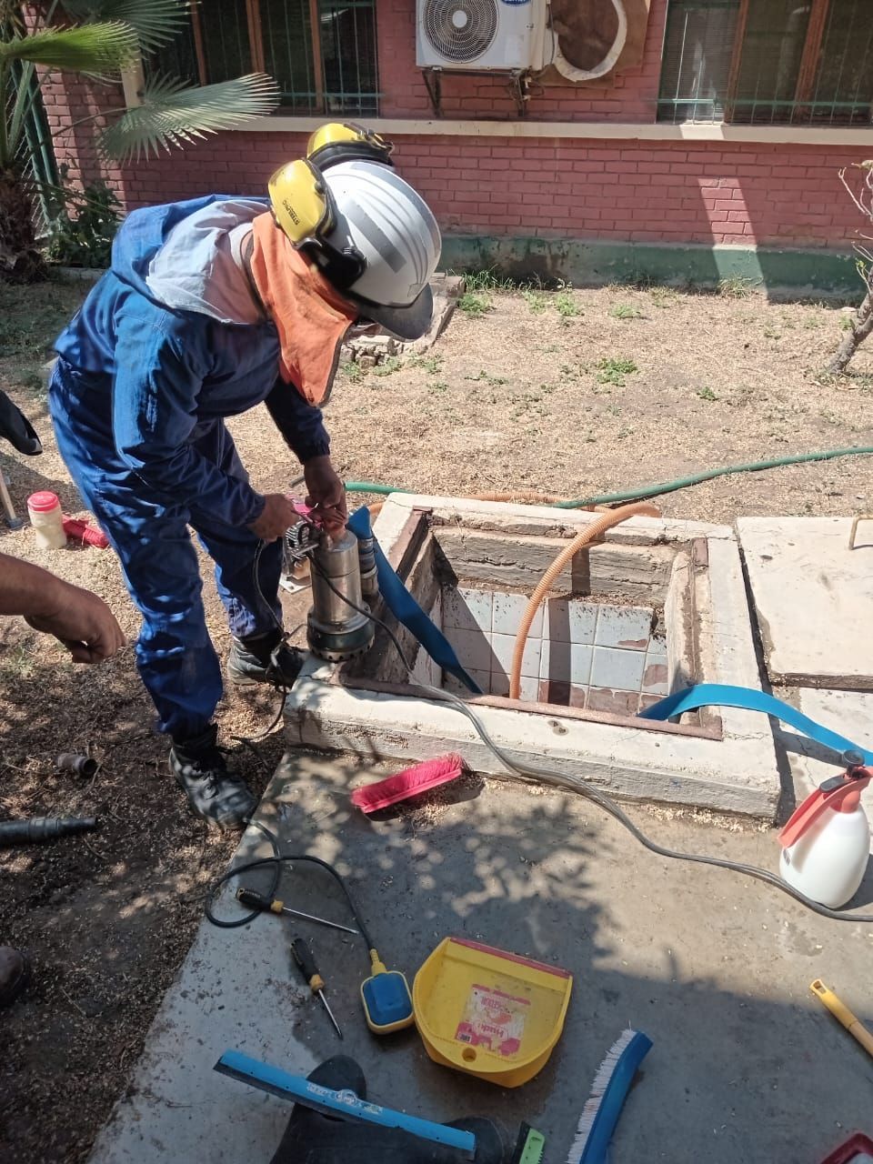 Obrero con traje de seguridad azul utilizando herramientas junto a una zanja abierta en una obra de construcción.