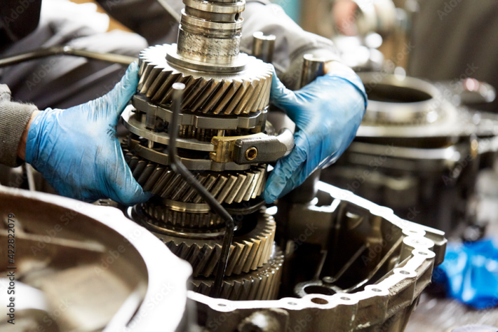 Mani guantate che assemblano ingranaggi metallici all'interno di una trasmissione su un banco da lavoro.