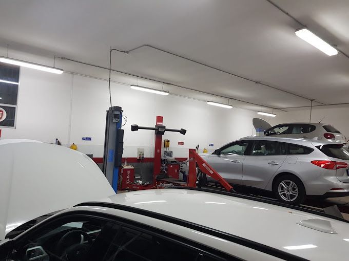 Officina meccanica con auto sui ponti sollevatori e veicoli coperti in un garage luminoso.