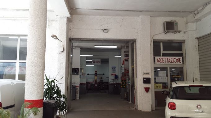 Ingresso del parcheggio con pilastri bianchi, una piccola auto sulla destra e un cartello con la scritta