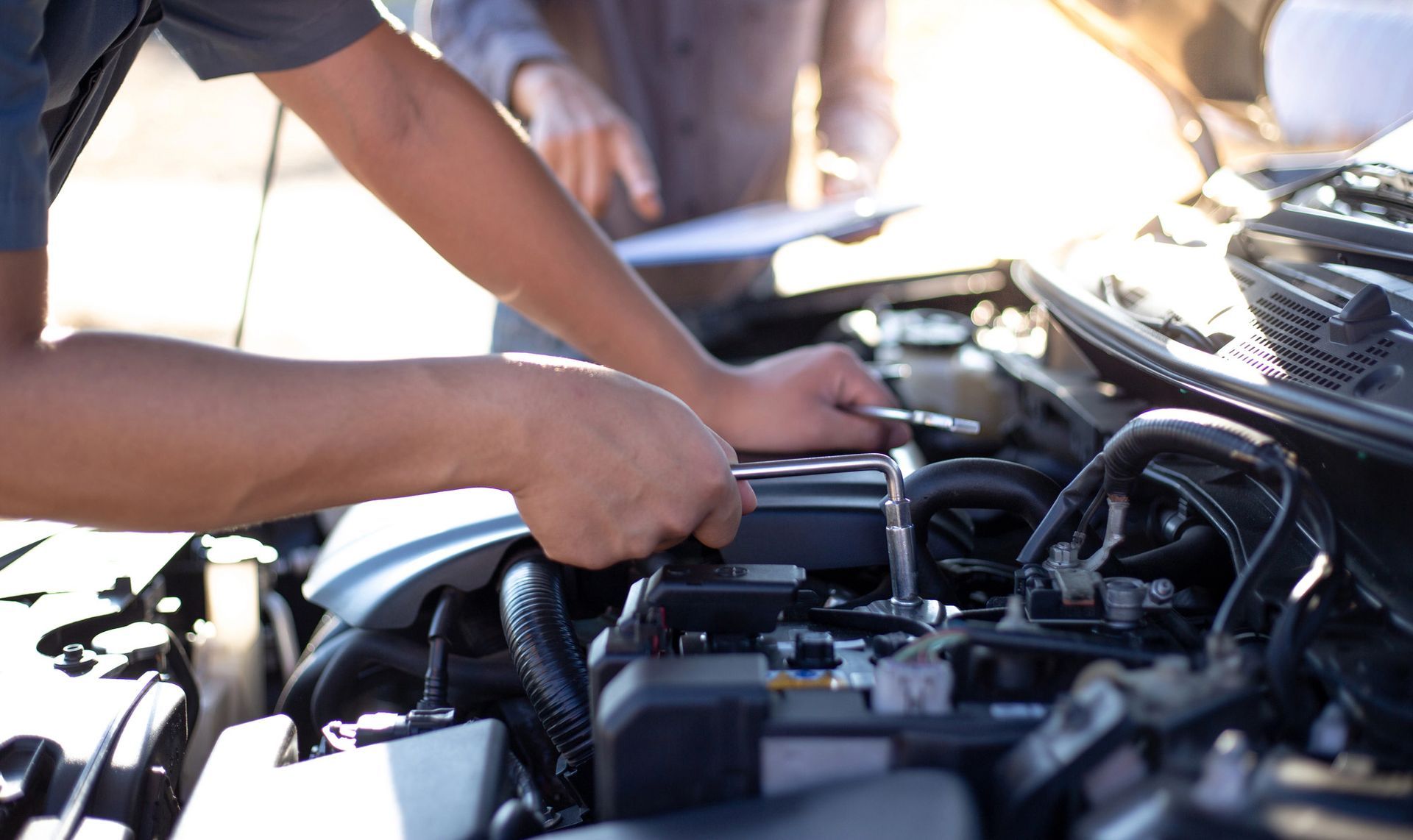Mani al lavoro sotto il cofano di un'auto, intente a riparare il motore in pieno giorno.