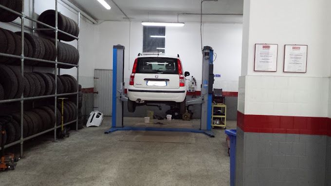 Un SUV bianco su un ponte sollevatore in un'officina meccanica, con pneumatici impilati e attrezzature da garage.