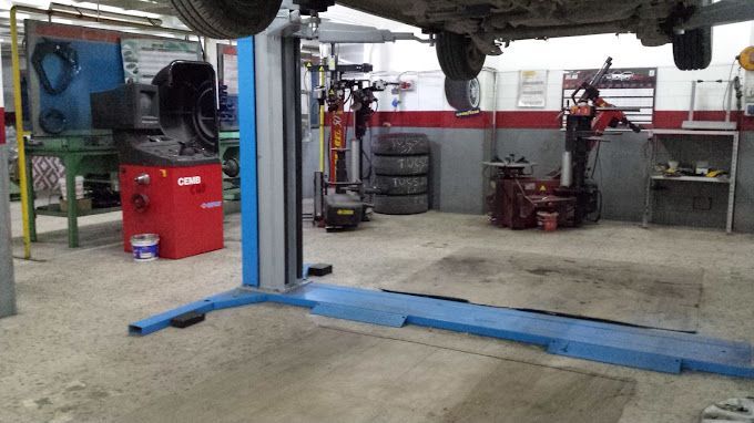 Officina meccanica con un'auto sollevata su un ponte sopra delle rampe blu e pneumatici accatastati nelle vicinanze.