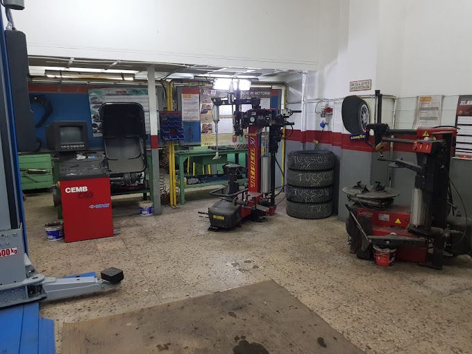 Officina meccanica con ponti sollevatori, pneumatici e carrelli portautensili in un garage disordinato.
