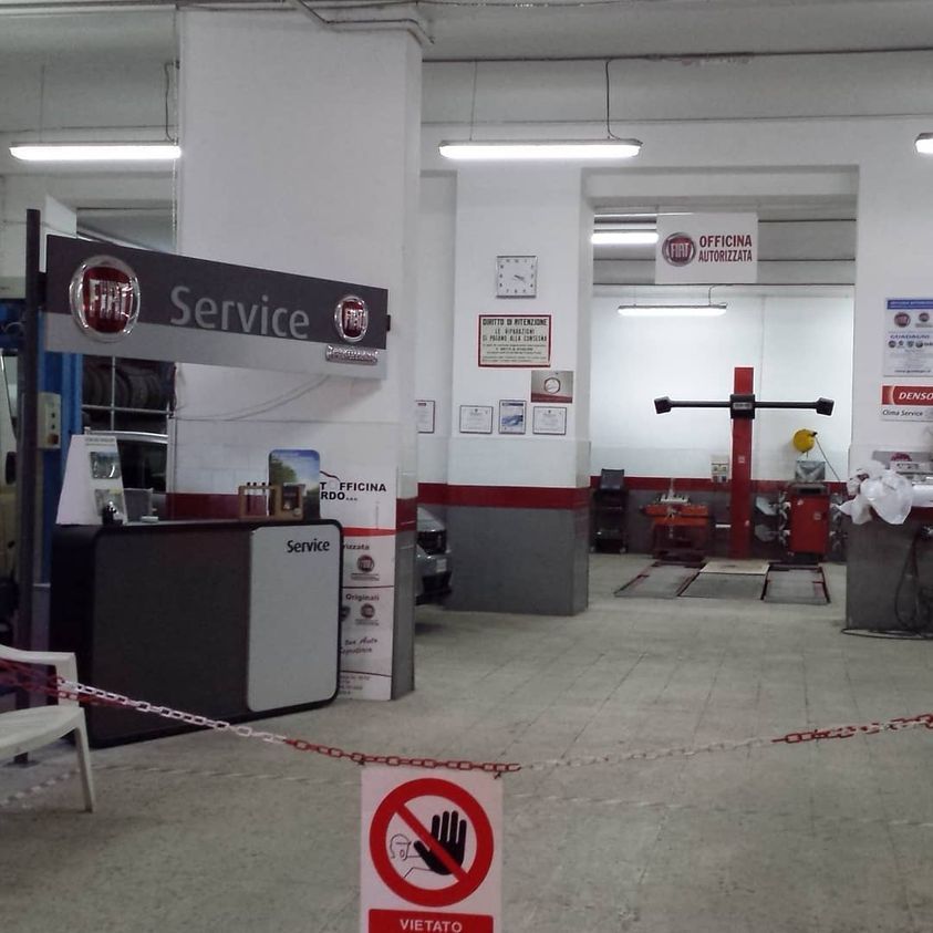 Interno di un'officina meccanica con banco di servizio, sollevatore e barriere a catena sul pavimento.