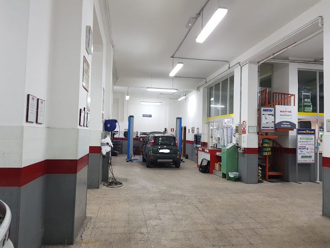 Postazione di riparazione auto con un'auto sul ponte sollevatore, attrezzi e pareti bianche brillanti con finiture rosse.