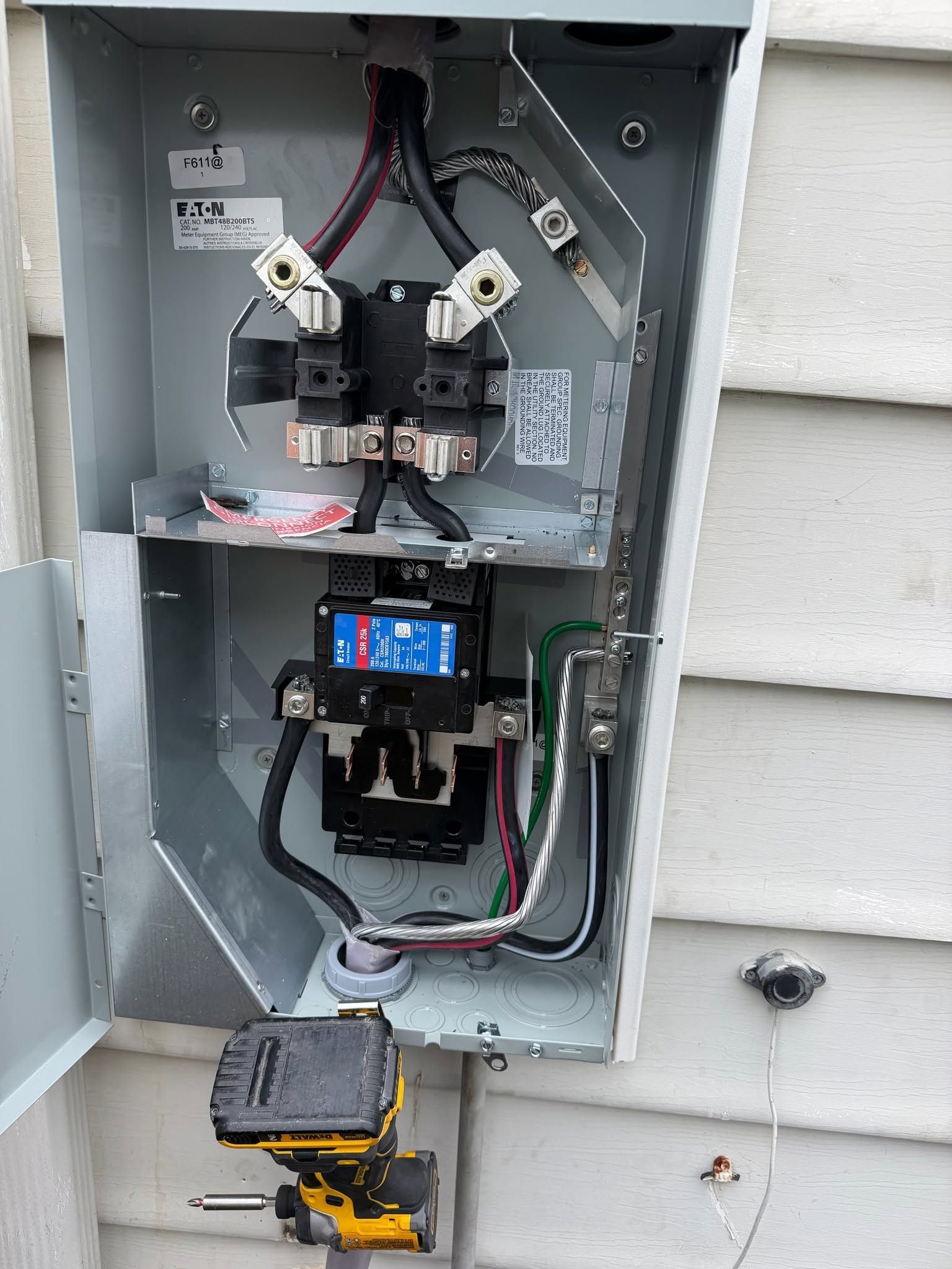 Open electrical meter panel with wires, breakers, and a yellow power tool below.