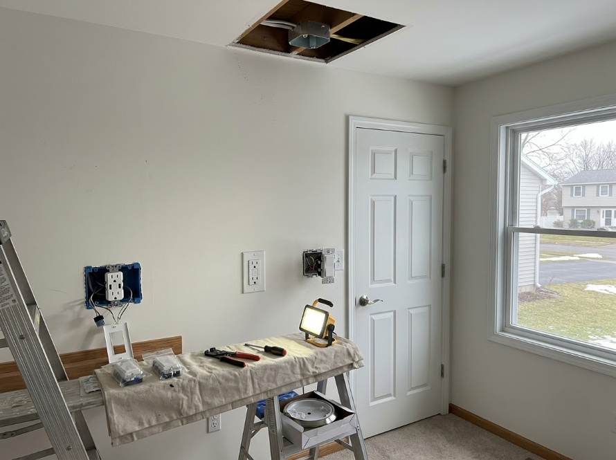 Partially renovated room with ladder, workbench, exposed ceiling, and large window.