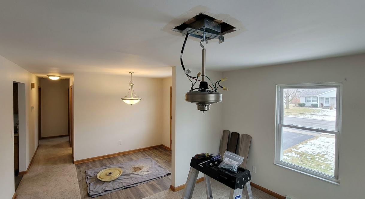 Unfinished room with exposed ceiling light fixture, ladder, and tools near a window and hallway.