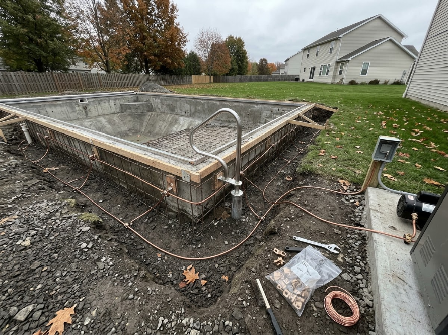 Backyard in-ground pool under construction beside a house, with muddy ground and framing exposed