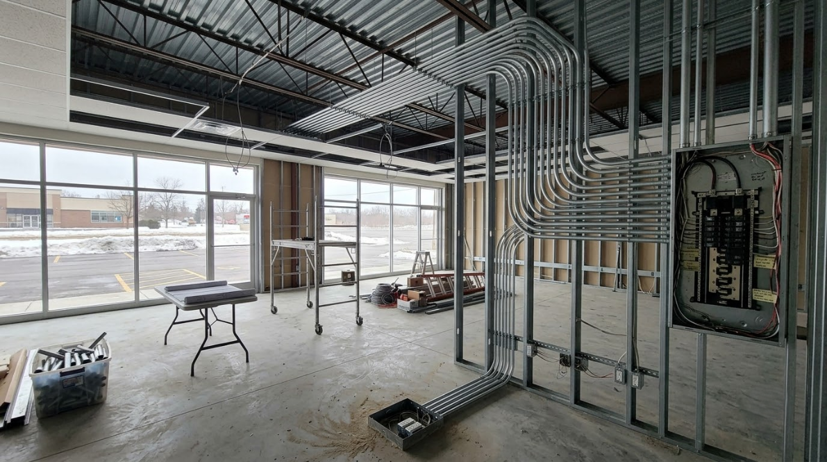 Unfinished office interior with exposed framing, ducts, and large windows overlooking a snowy street.
