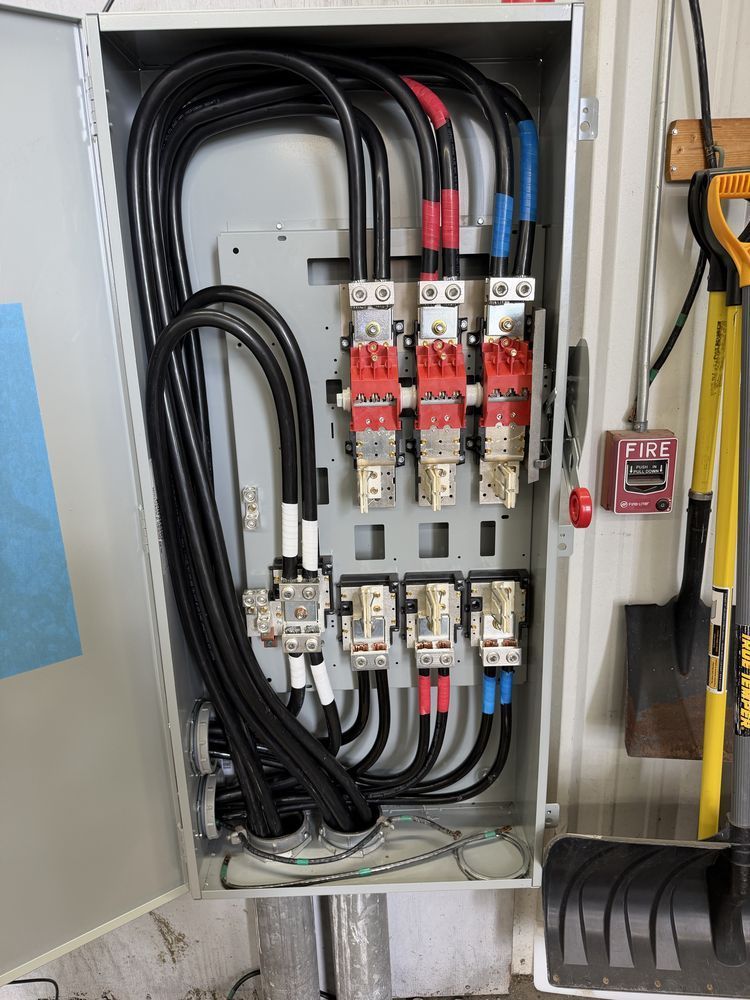 Open electrical panel with thick black and red cables and circuit breakers inside a gray metal cabinet