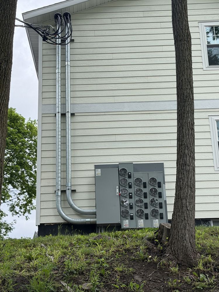Exterior wall of a house with utility pipes, electrical equipment, and a tree in front