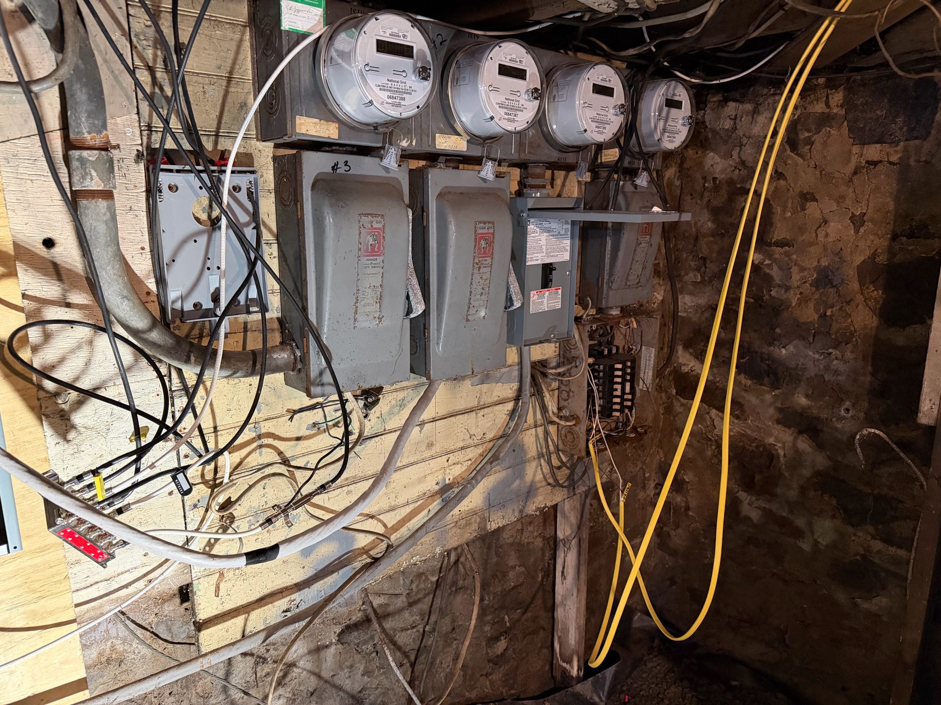 Electrical meter panel with exposed wiring and three utility meters mounted on a wall