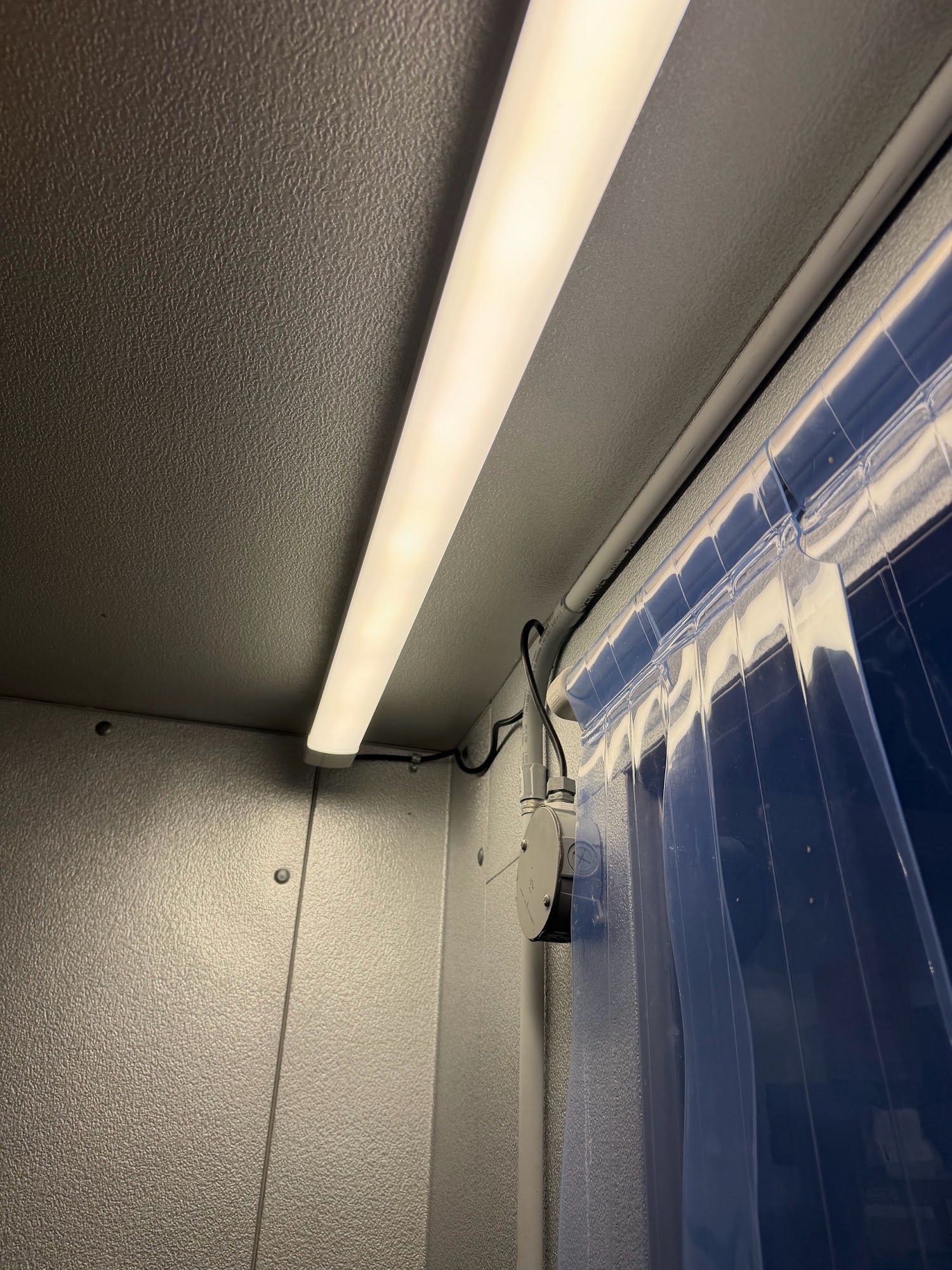 Close-up of a metal wall and ceiling corner with a fluorescent light and blue plastic curtain.