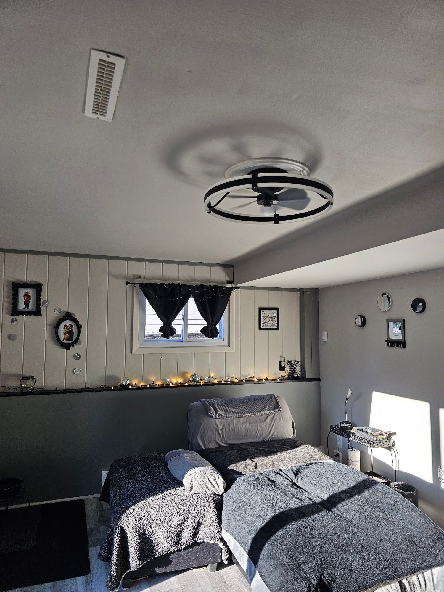 Cozy gray bedroom with a made bed, wall decor, a window with black curtains, and a ceiling light chandelier