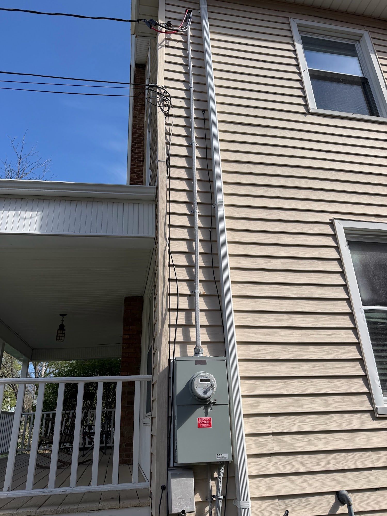 House side wall with utility meter, cable lines, and a covered porch against a blue sky.