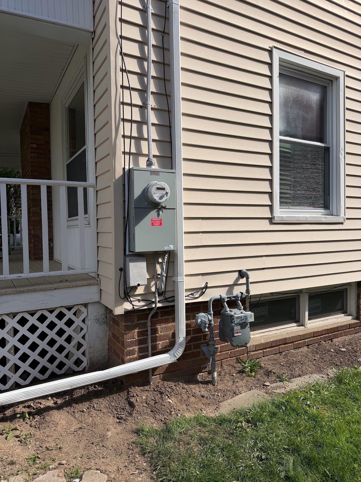 House exterior with electric meter, conduit, and utility lines beside a porch and basement window
