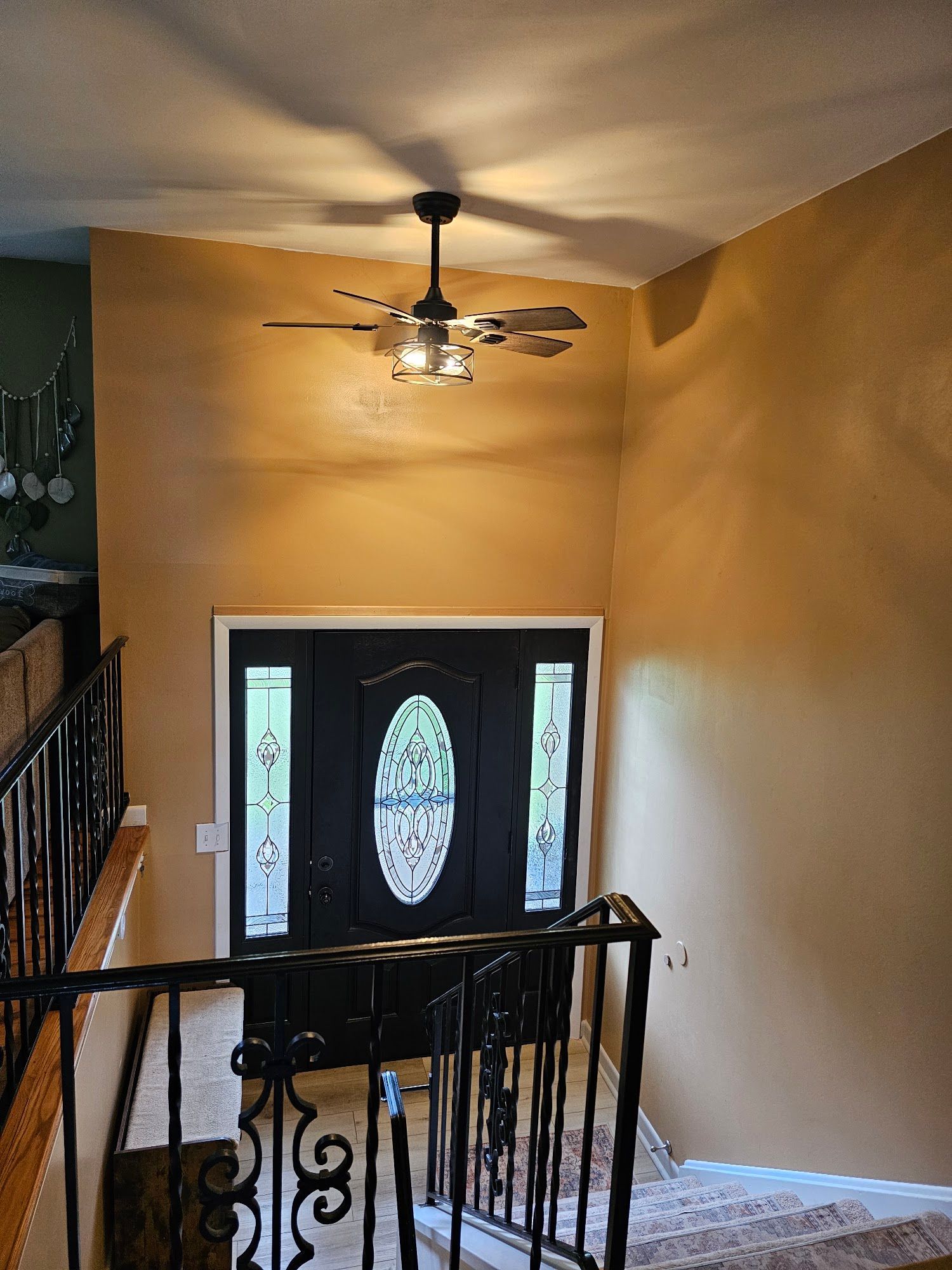 Stair landing with black railing, white front door, warm tan walls, and a ceiling fan overhead
