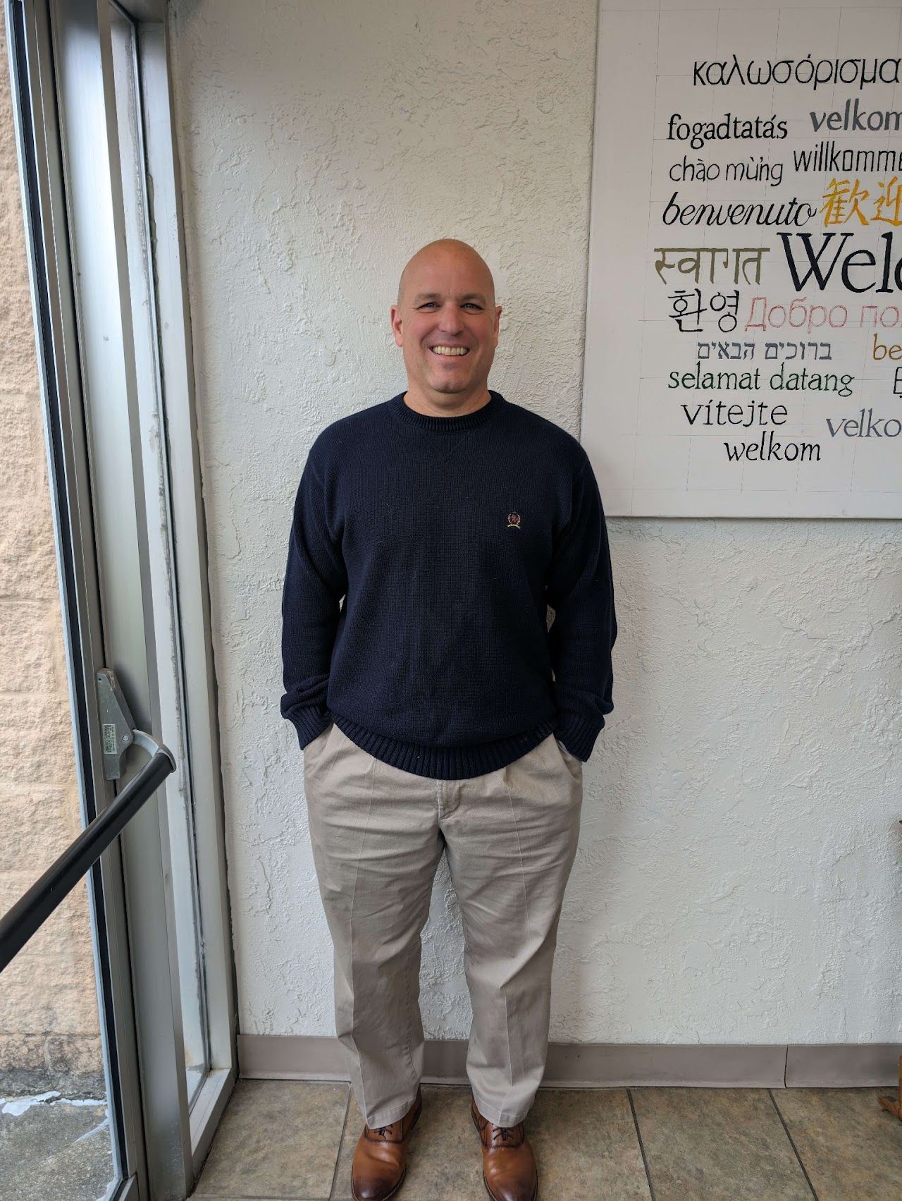 A man in a black sweater and khaki pants is standing in front of a sign.