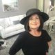 Woman in black hat and sweater smiles indoors, near sofa.