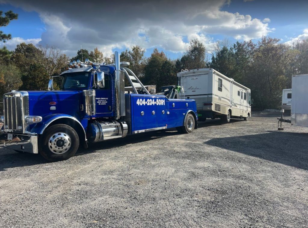 A blue tow truck is towing a rv in a gravel lot.