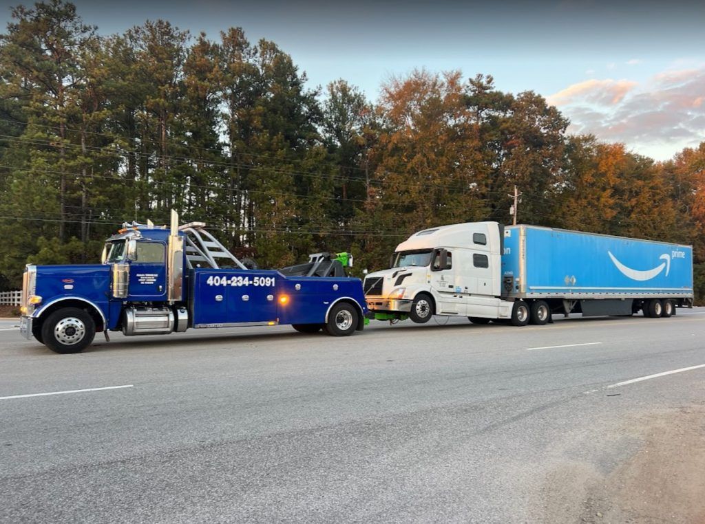 A blue tow truck is pulling a blue amazon semi truck