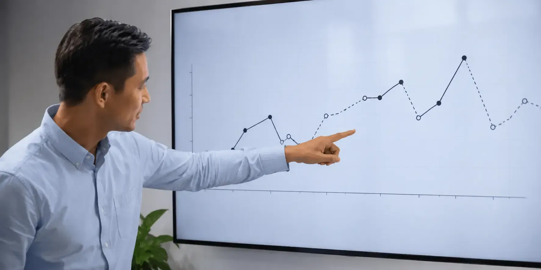 Person pointing to a digital chart with missing data points on a large office screen.