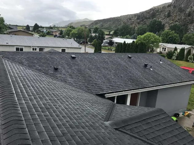 Dark gray shingle roof on a suburban home with mountains and cloudy sky in the background