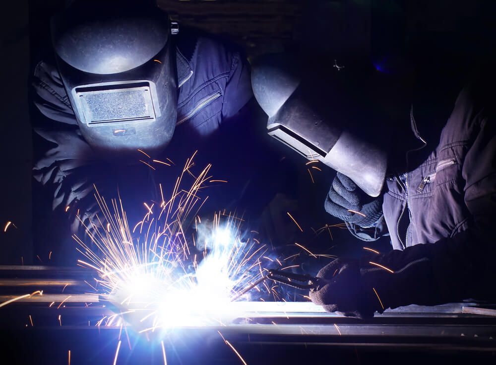 Two Welders, Sparks Flying, Welding Metal Together In A Dark Workshop